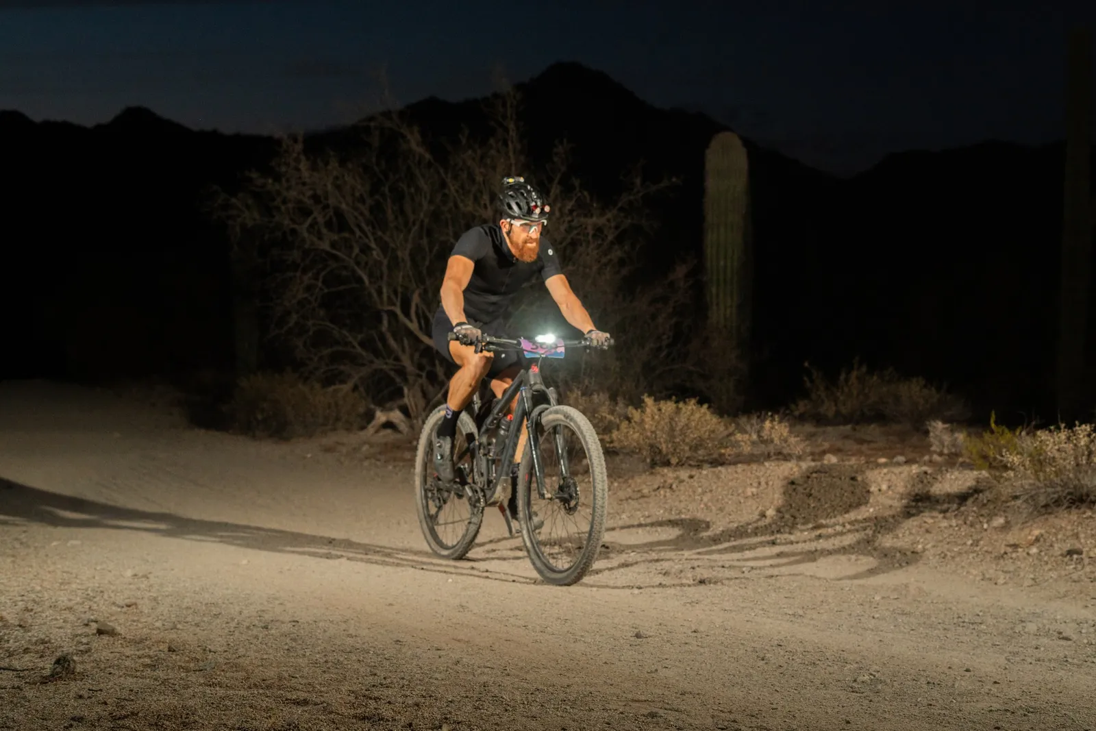 Rider by bike light among the saguaros at the Sinister Night Rides in San Tan Mountain Regional Park