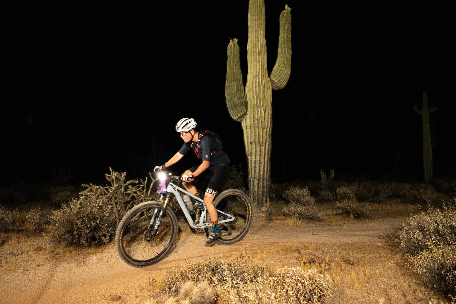 Rider by bike light past a saguaro at the Adrenaline Night Rides in McDowell Mountain Regional Park