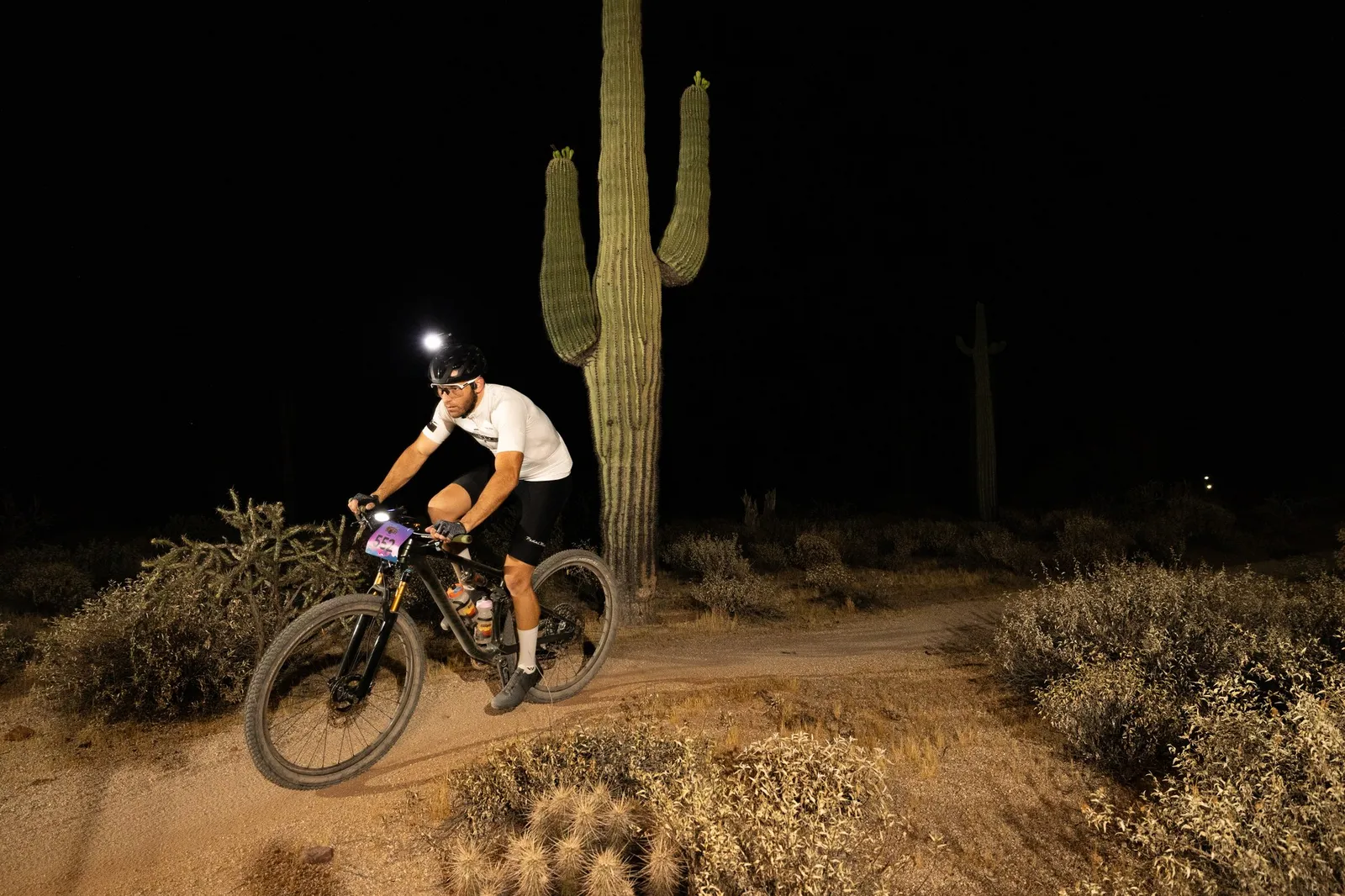 Rider by bike light past a saguaro at the Adrenaline Night Rides in McDowell Mountain Regional Park