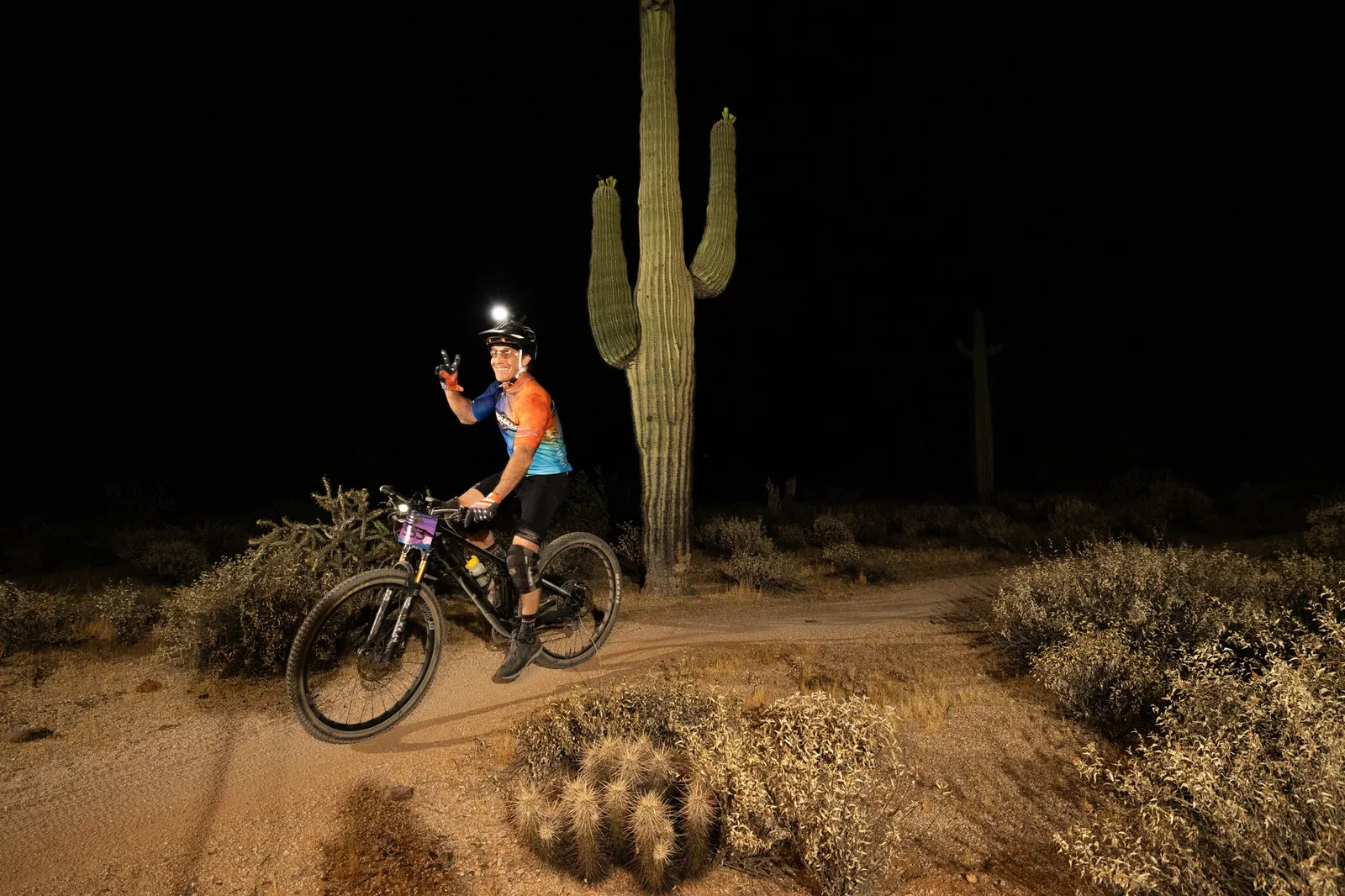 Rider by bike light past a saguaro at the Adrenaline Night Rides in McDowell Mountain Regional Park