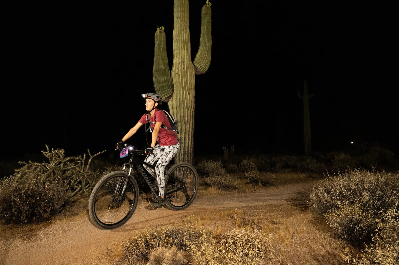 Rider by bike light past a saguaro at the Adrenaline Night Rides in McDowell Mountain Regional Park