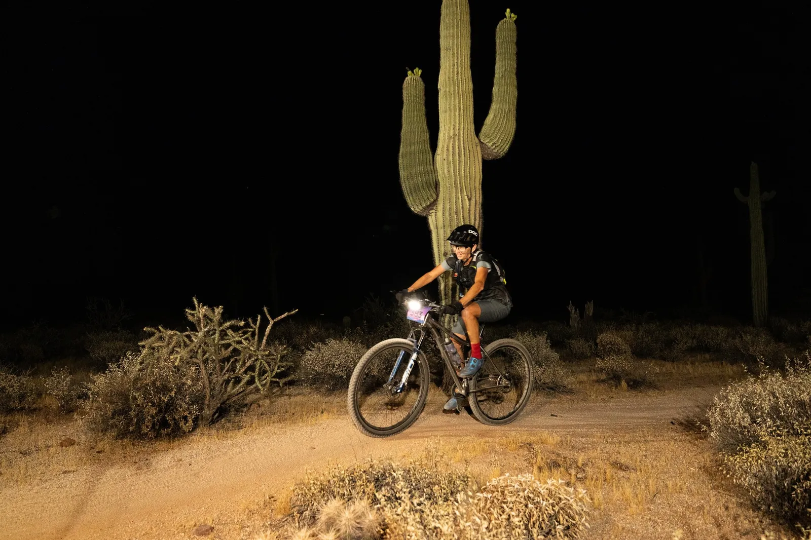 Rider by bike light past a saguaro at the Adrenaline Night Rides in McDowell Mountain Regional Park