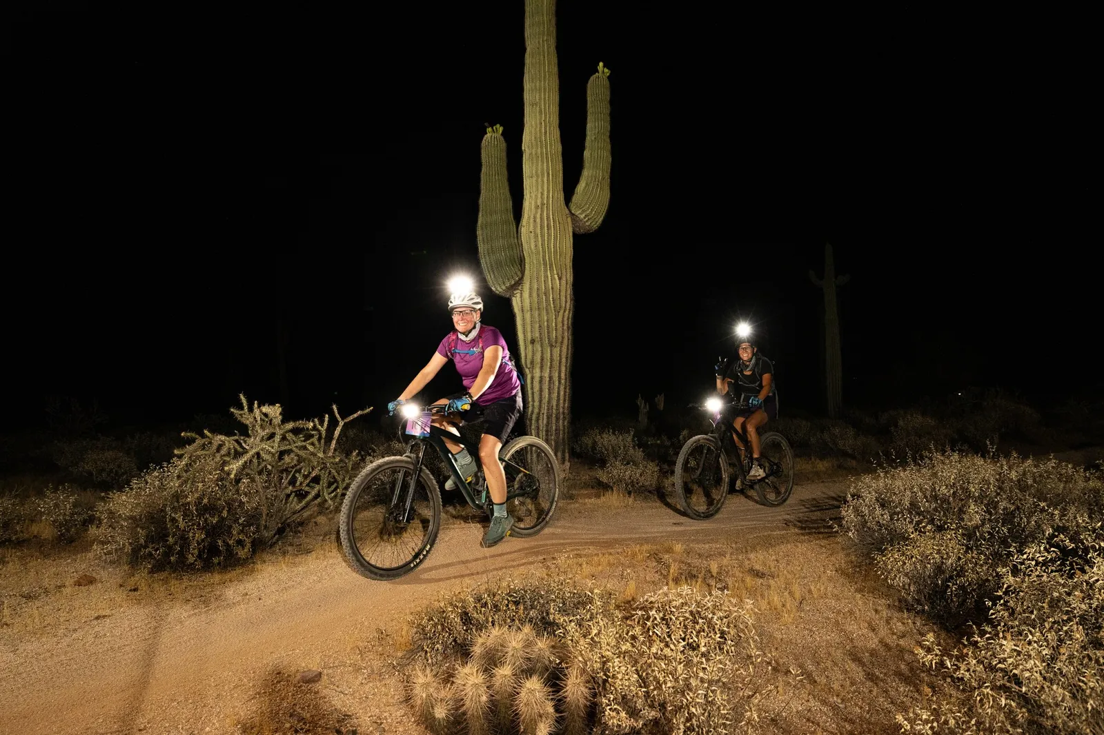 Rider by bike light past a saguaro at the Adrenaline Night Rides in McDowell Mountain Regional Park