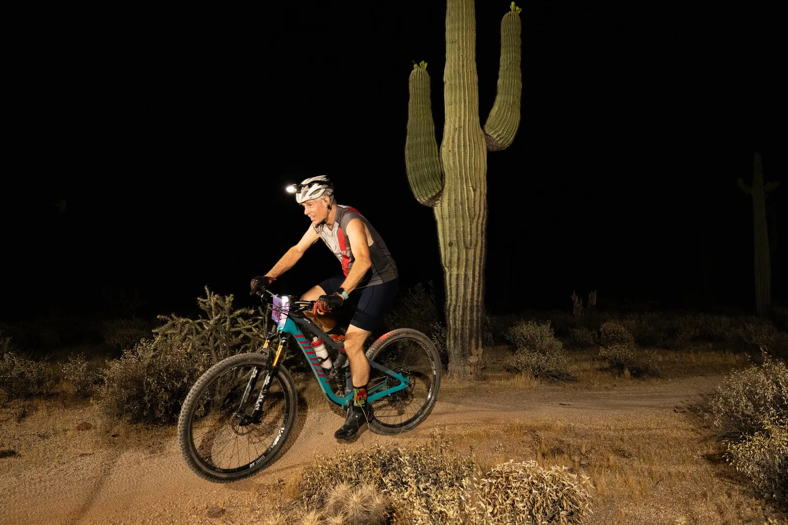 Rider by bike light past a saguaro at the Adrenaline Night Rides in McDowell Mountain Regional Park