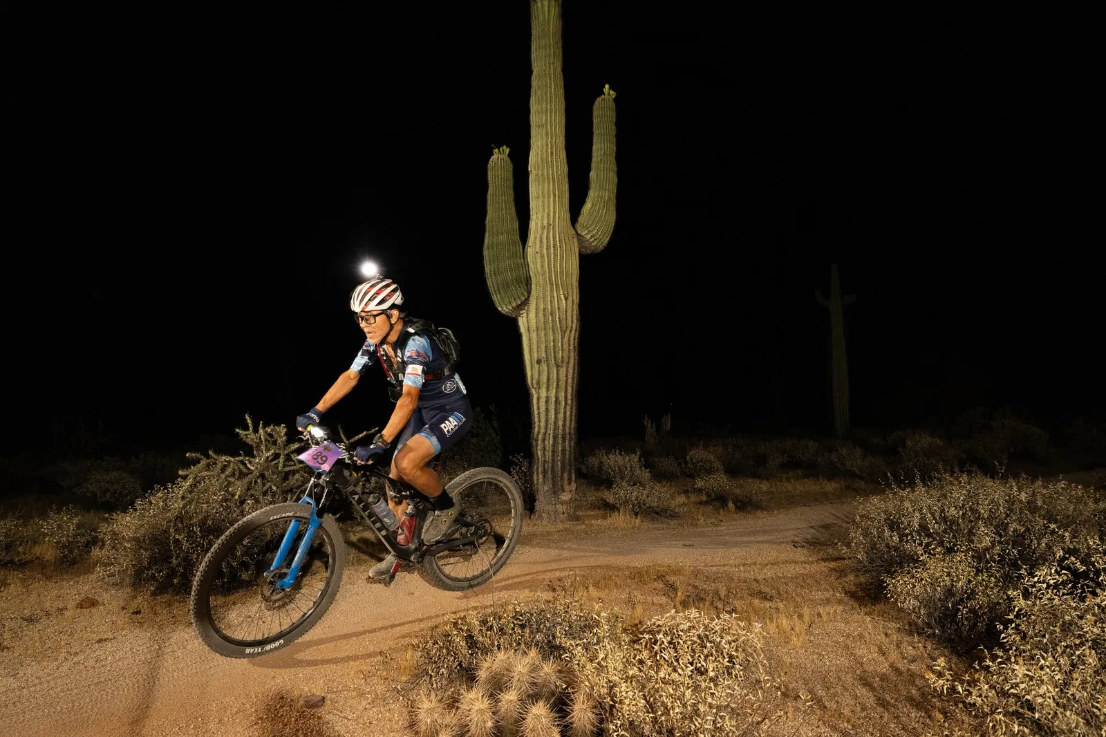 Rider by bike light past a saguaro at the Adrenaline Night Rides in McDowell Mountain Regional Park