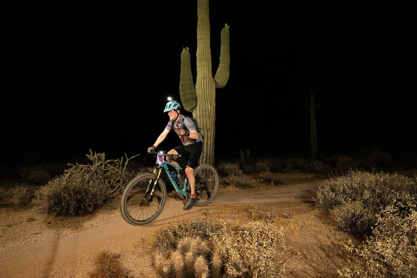Rider by bike light past a saguaro at the Adrenaline Night Rides in McDowell Mountain Regional Park