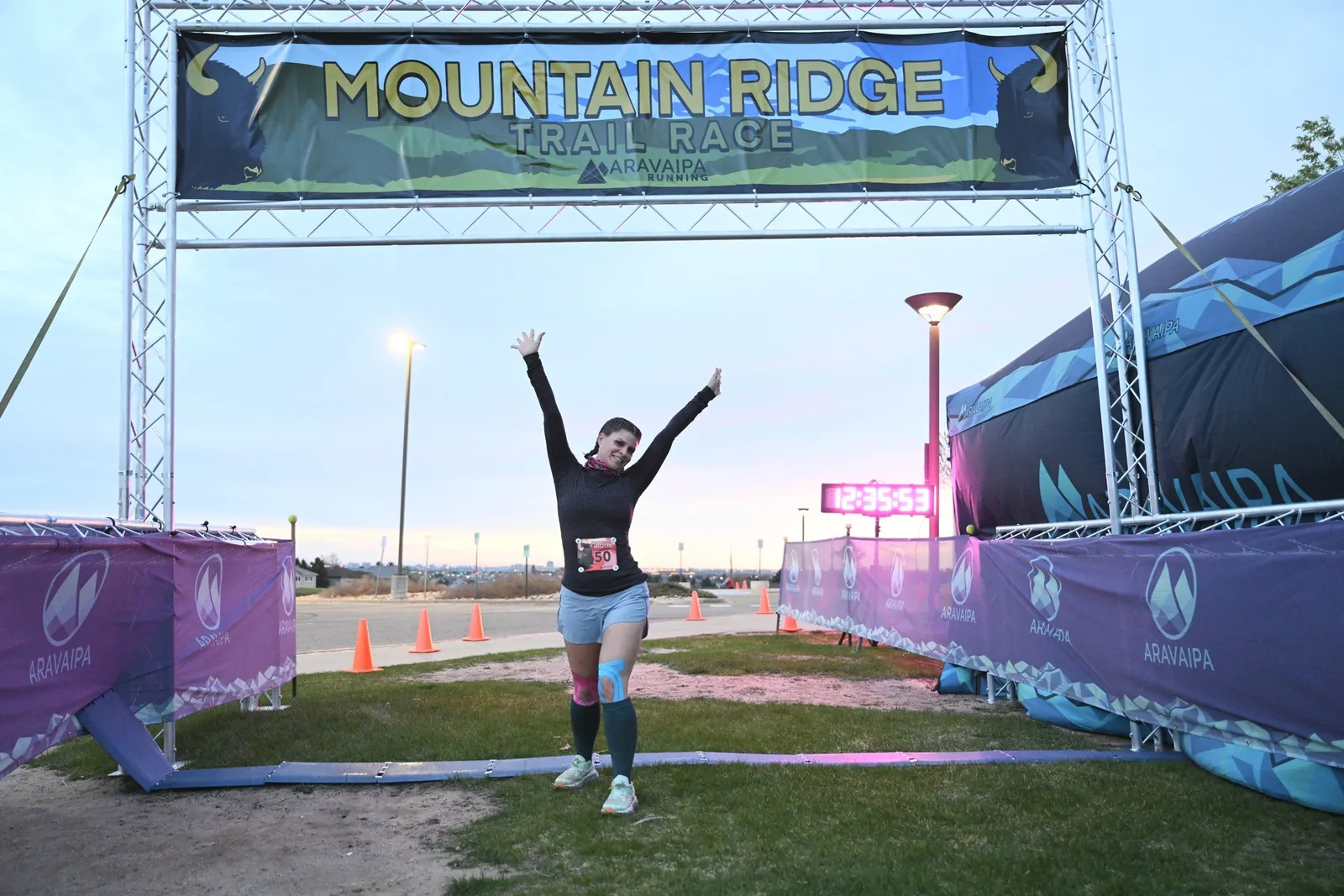 A runner with arms raised under the Mountain Ridge arch