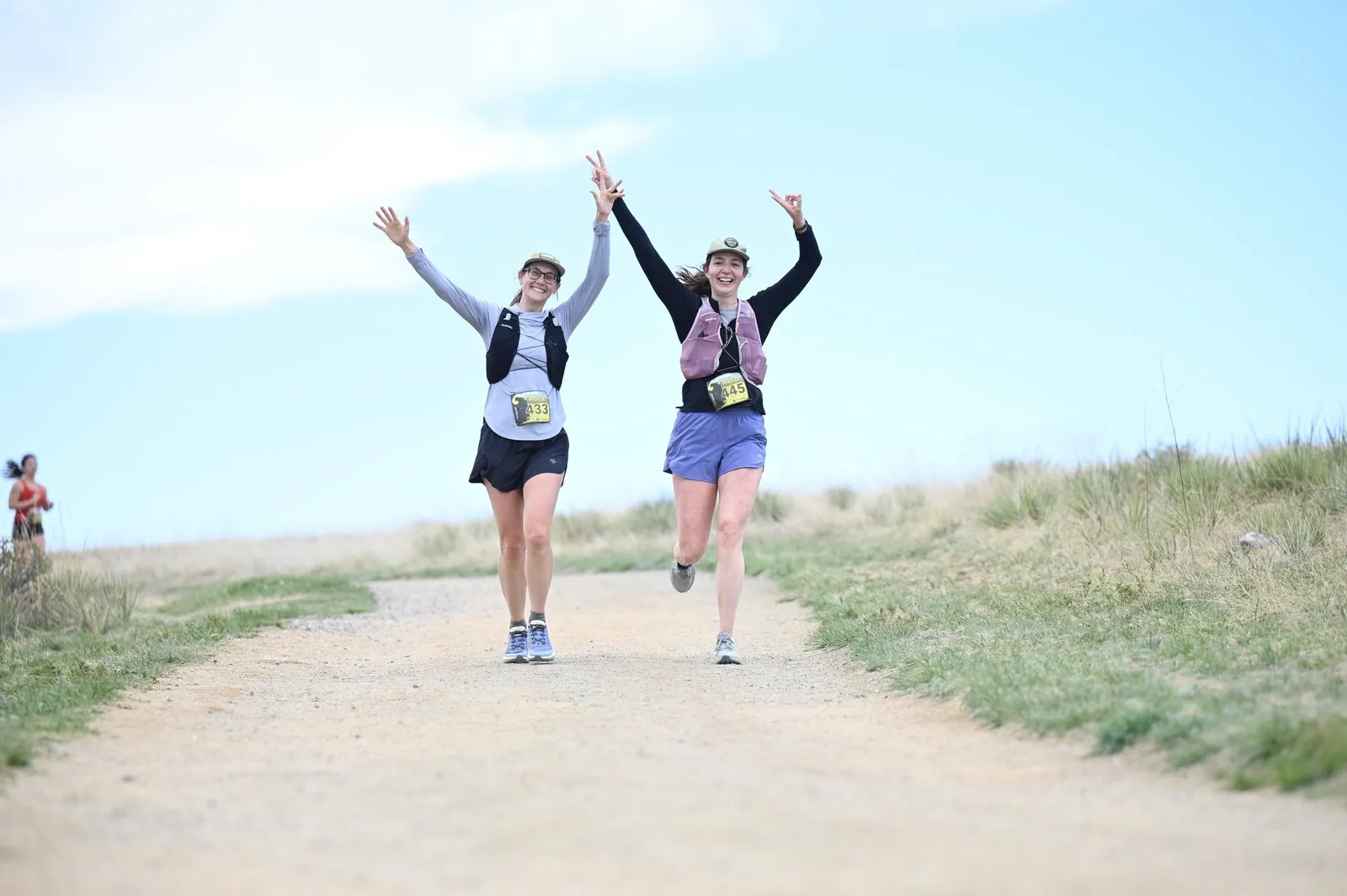 Two runners waving on the dirt trail