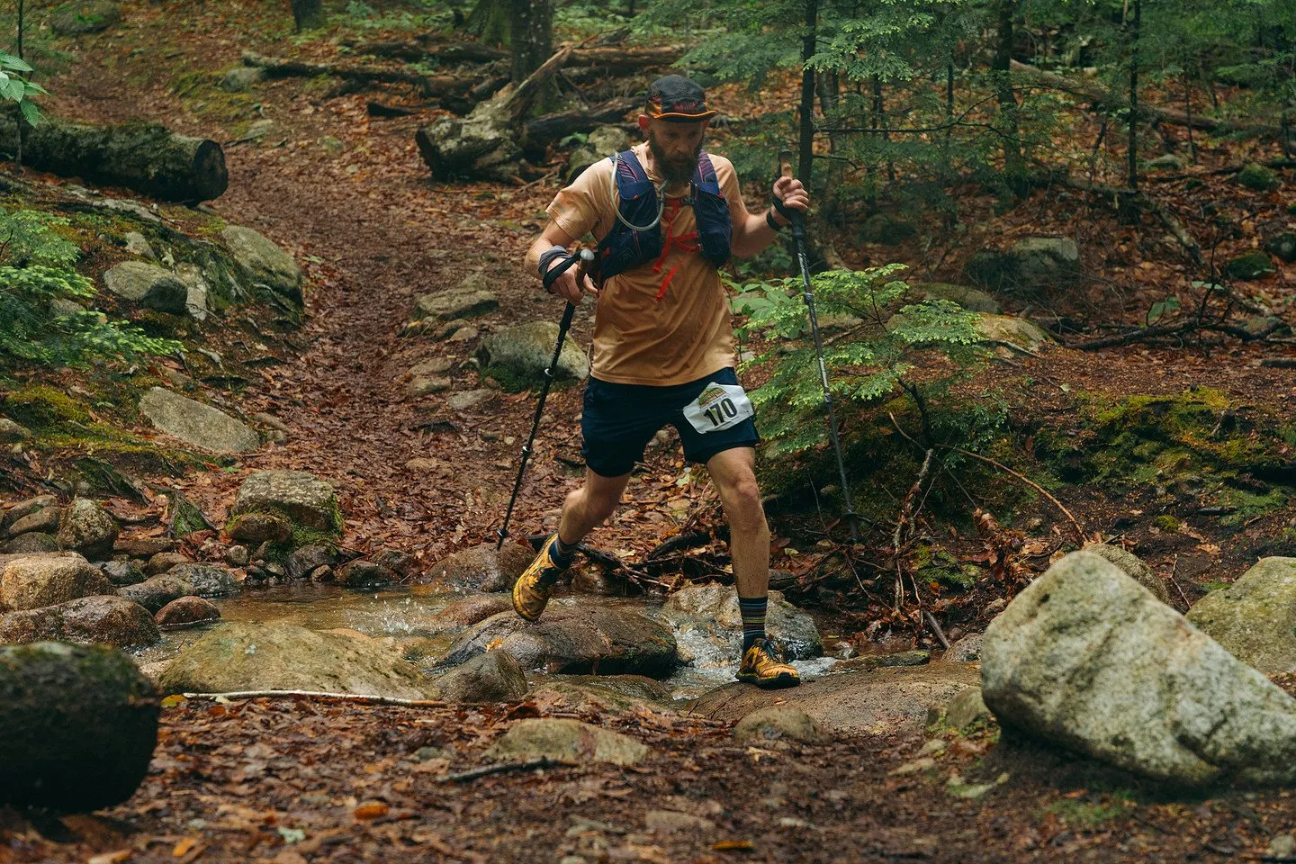 A runner with poles crossing a rocky stream