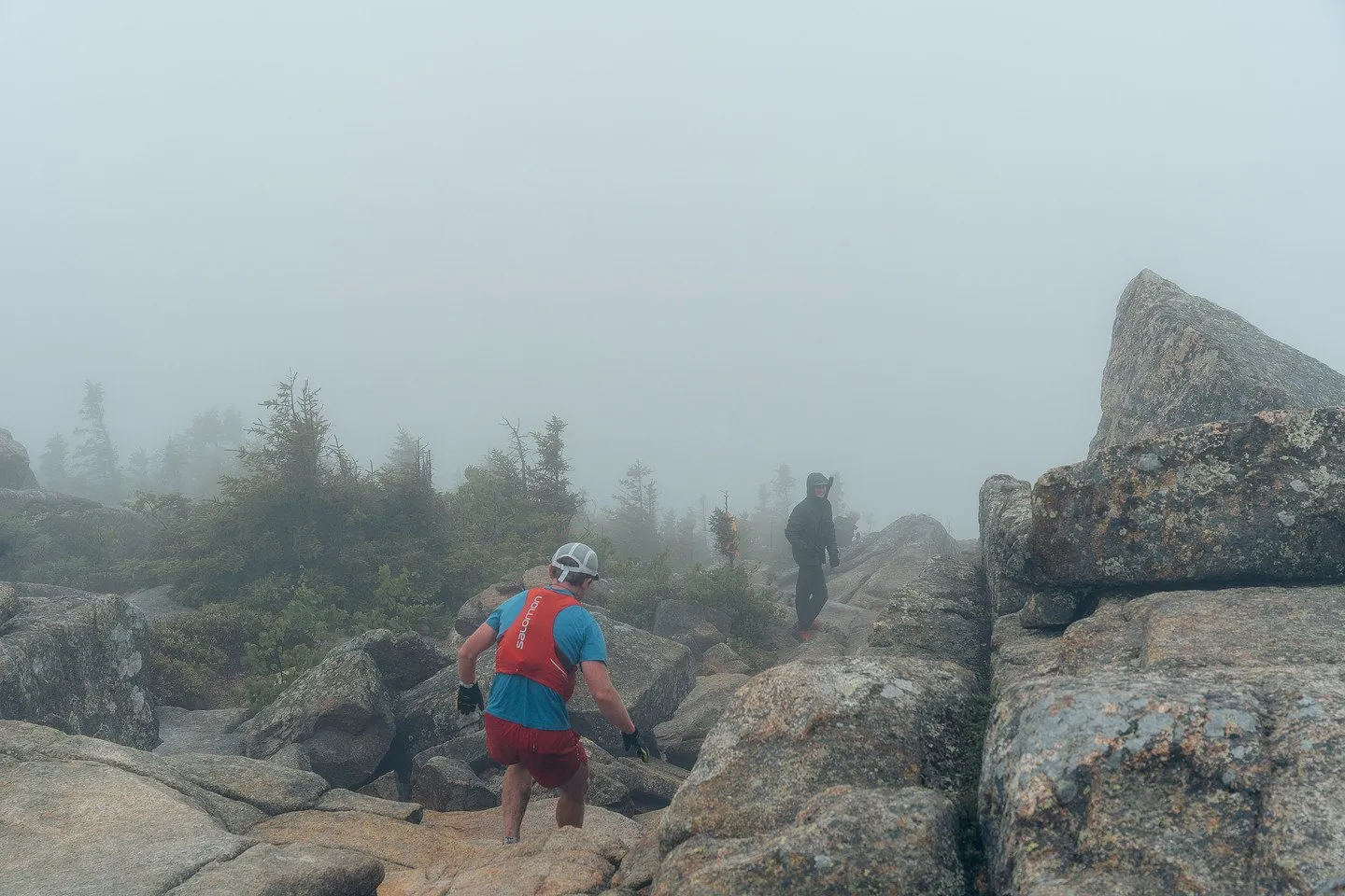 Runners scrambling the summit rocks in the fog