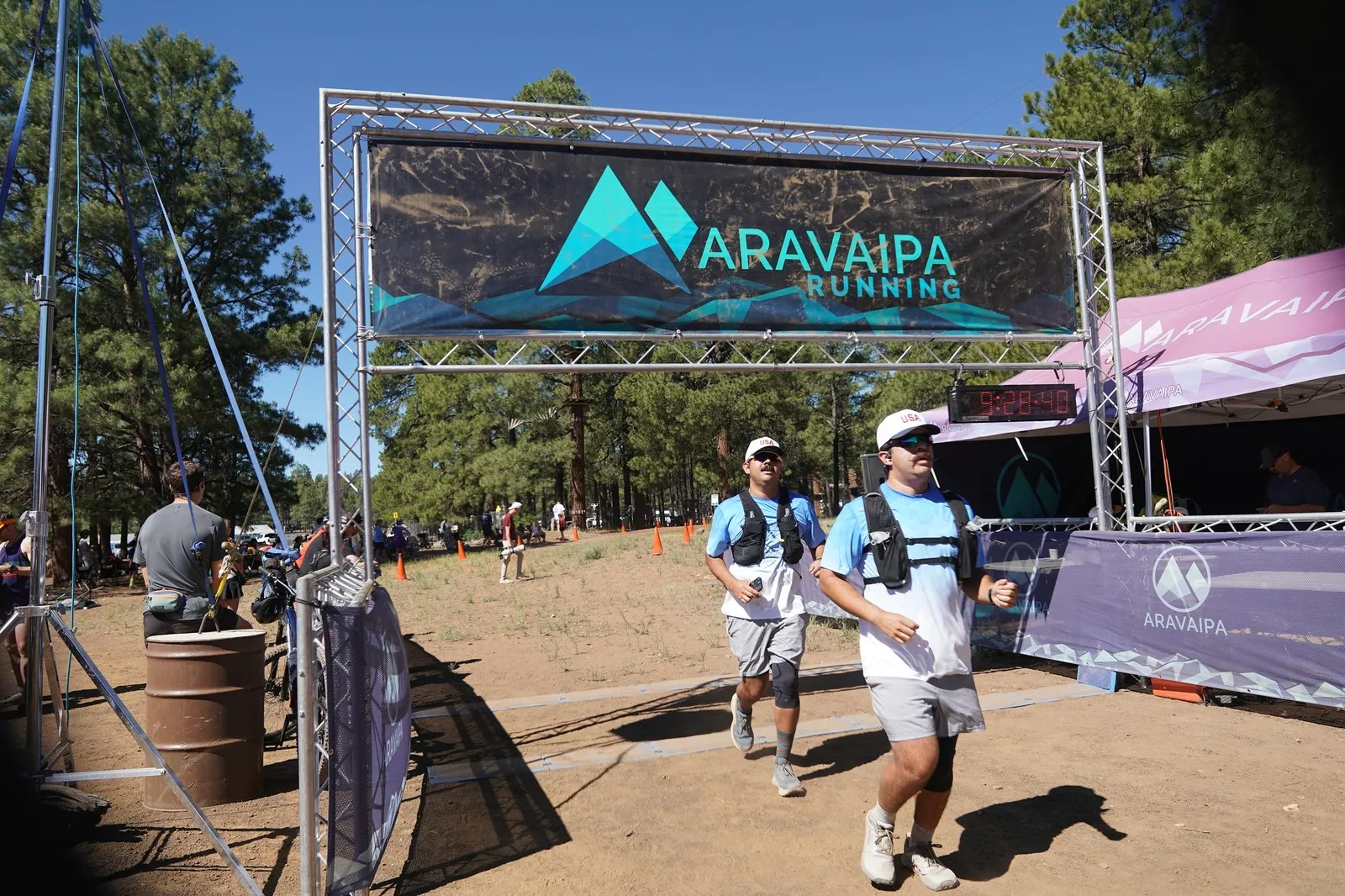 Two runners in light blue at the Big Pine Trail Runs finish line in the Flagstaff ponderosa pines