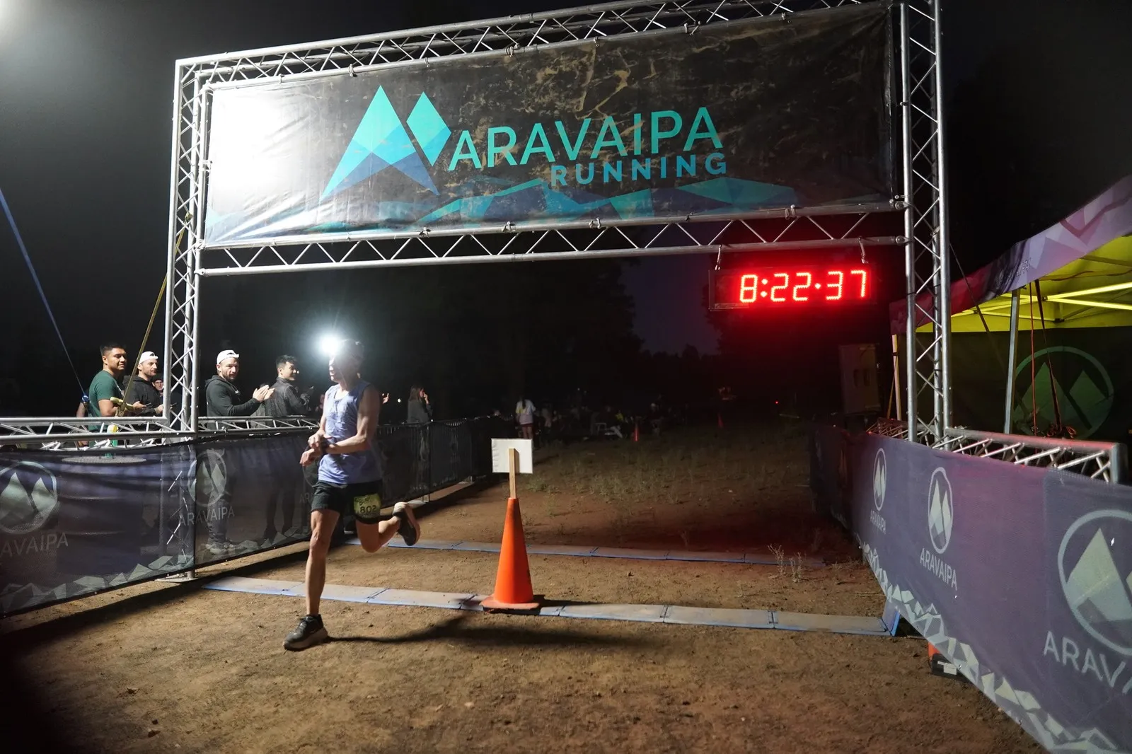 A runner with a headlamp sprinting into the Blackout Night Runs finish line in the Flagstaff pines