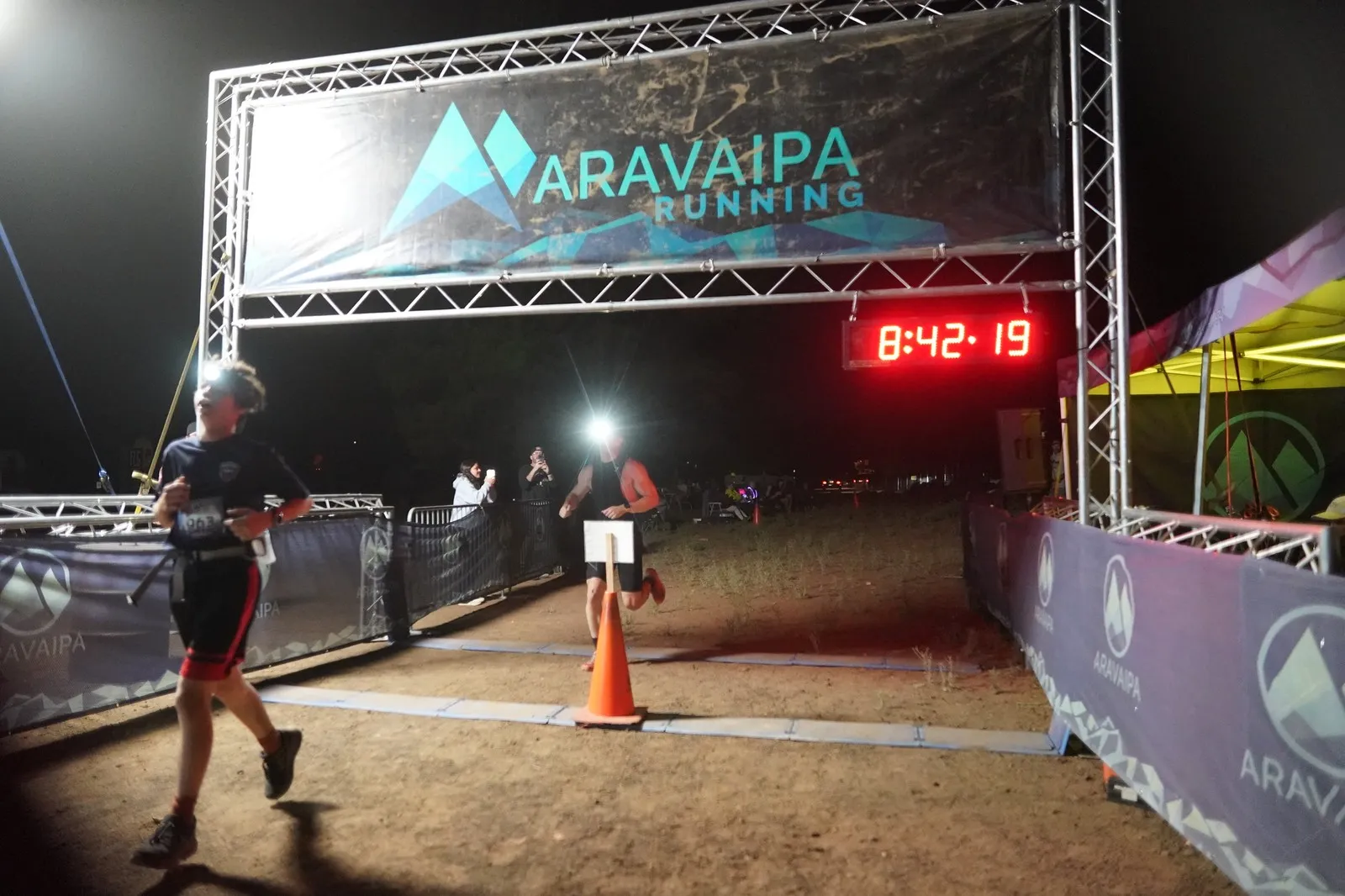 Two runners finishing at the Blackout Night Runs finish line in the Flagstaff pines