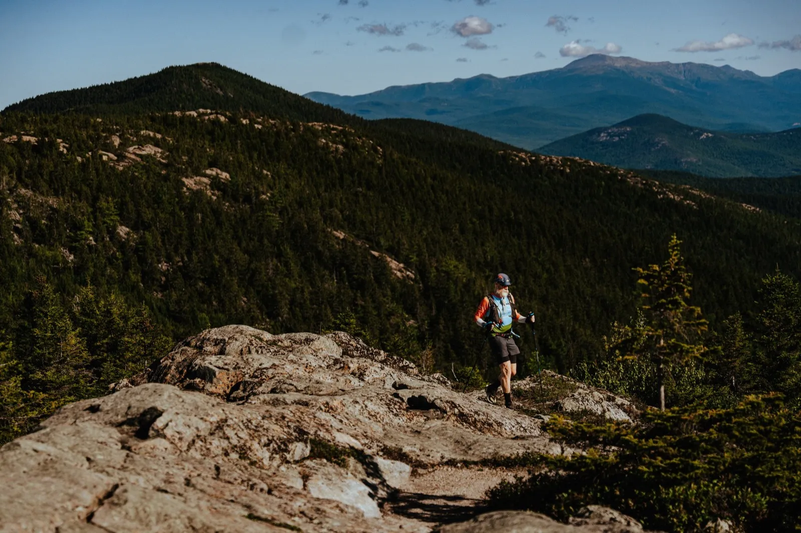 A runner crosses the high granite ridge with the high peaks on the horizon