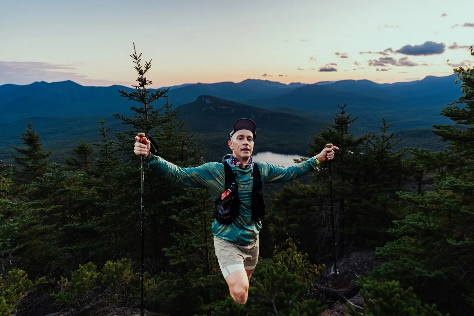 Arms flung wide on the ridge at dusk with the whole range behind