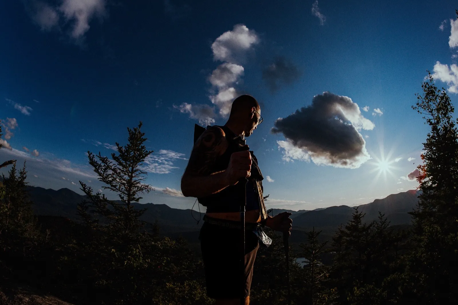 A runner in silhouette against the sun and clouds on the ridge
