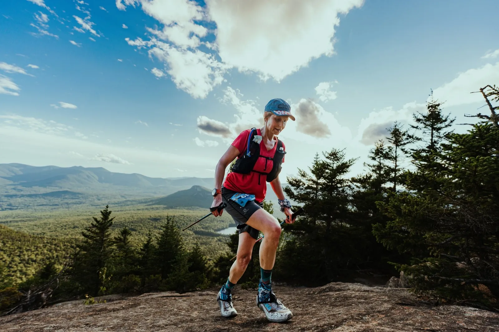 A runner bounds across the summit ledge under a big afternoon sky