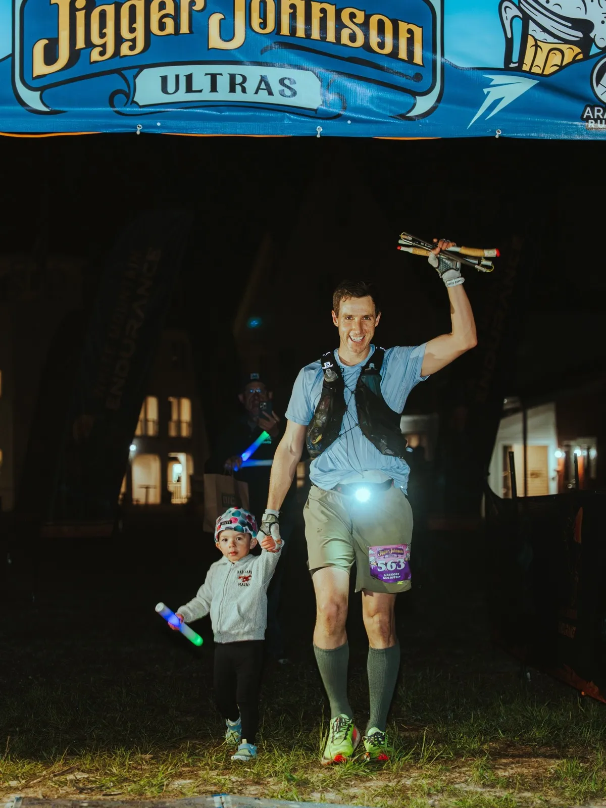 A finisher crosses the line at night with a little one at his side
