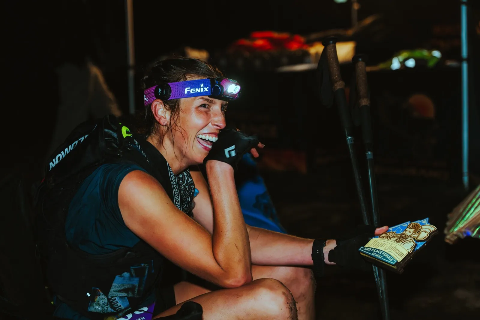 A 50 mile finisher laughs under her headlamp, award in hand