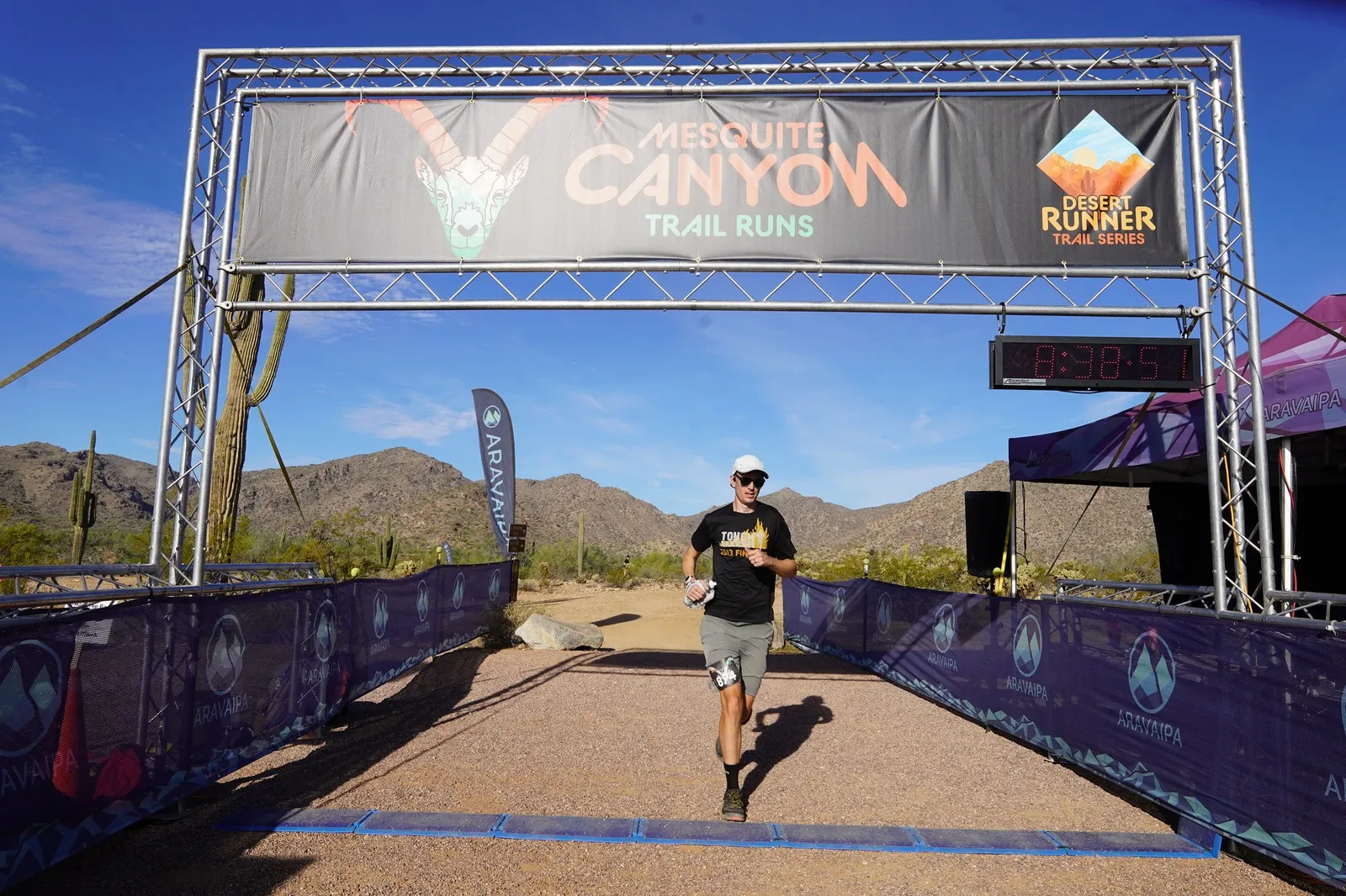 A runner finishing at the Mesquite Canyon Trail Runs finish line, a Sonoran Desert Cup race in White Tank Mountain Regional Park