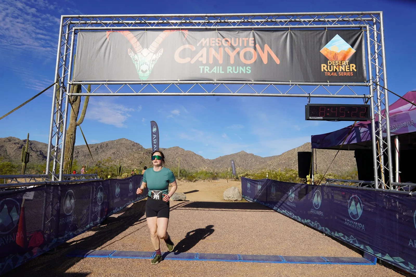 A runner in green at the Mesquite Canyon Trail Runs finish line, a Sonoran Desert Cup race in White Tank Mountain Regional Park