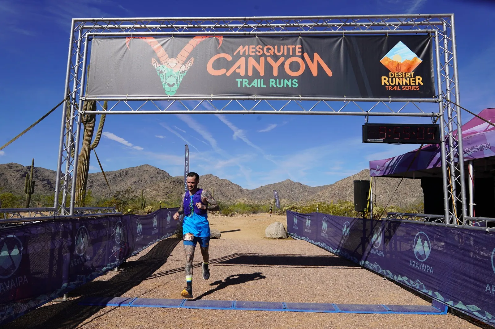 A runner in blue at the Mesquite Canyon Trail Runs finish line, a Sonoran Desert Cup race in White Tank Mountain Regional Park